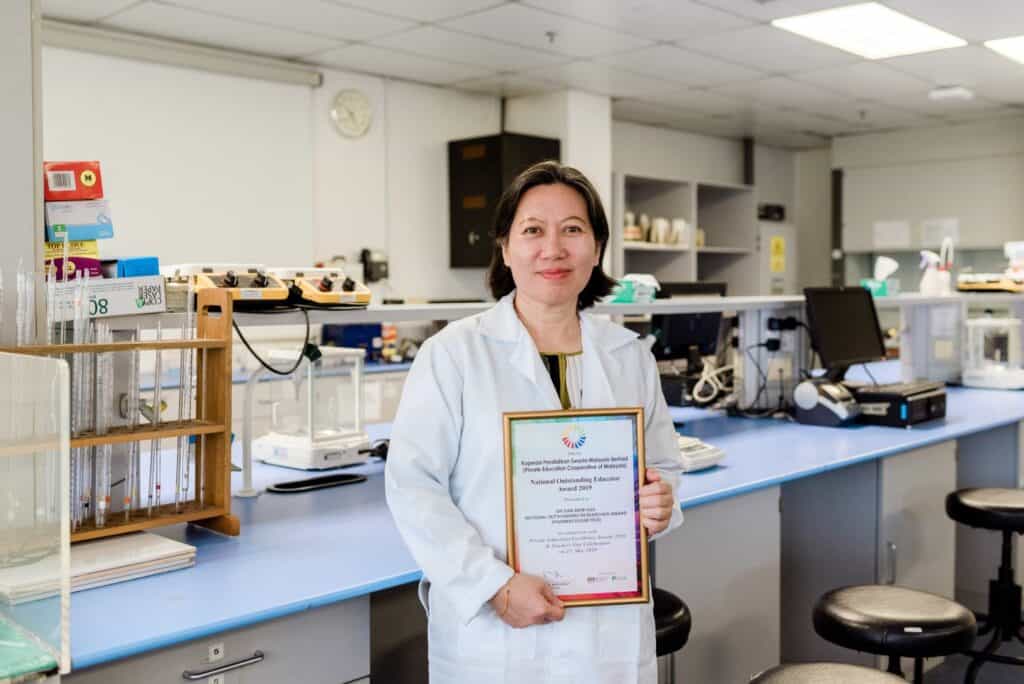 Prof. Dr. Gan Siew Hua holding a certificate of achievement in her laboratory at the University of Cyberjaya